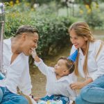 A joyful family celebrating their child's first birthday outdoors with cake and balloons.