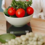 Colorful fresh vegetables including tomatoes and cucumbers on a kitchen scale for healthy eating.